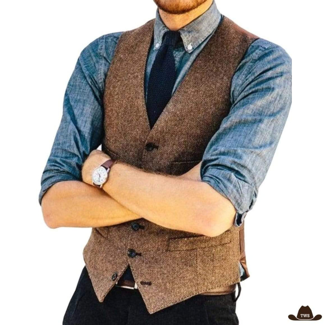 Man in brown tweed vest, blue shirt, dark tie, and watch with arms crossed.