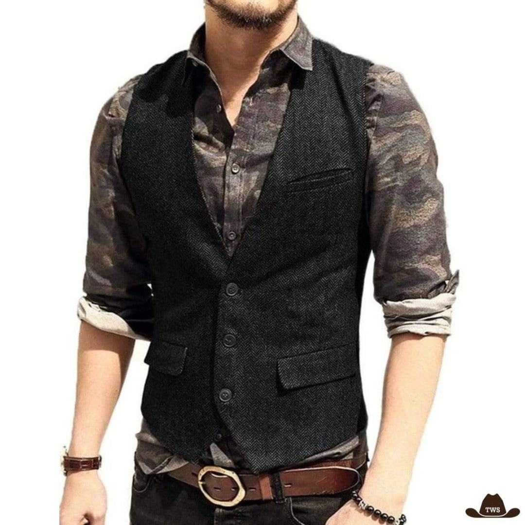 A man poses in a dark herringbone vest over a patterned button-down shirt, accented by a brown leather belt and accessories.
